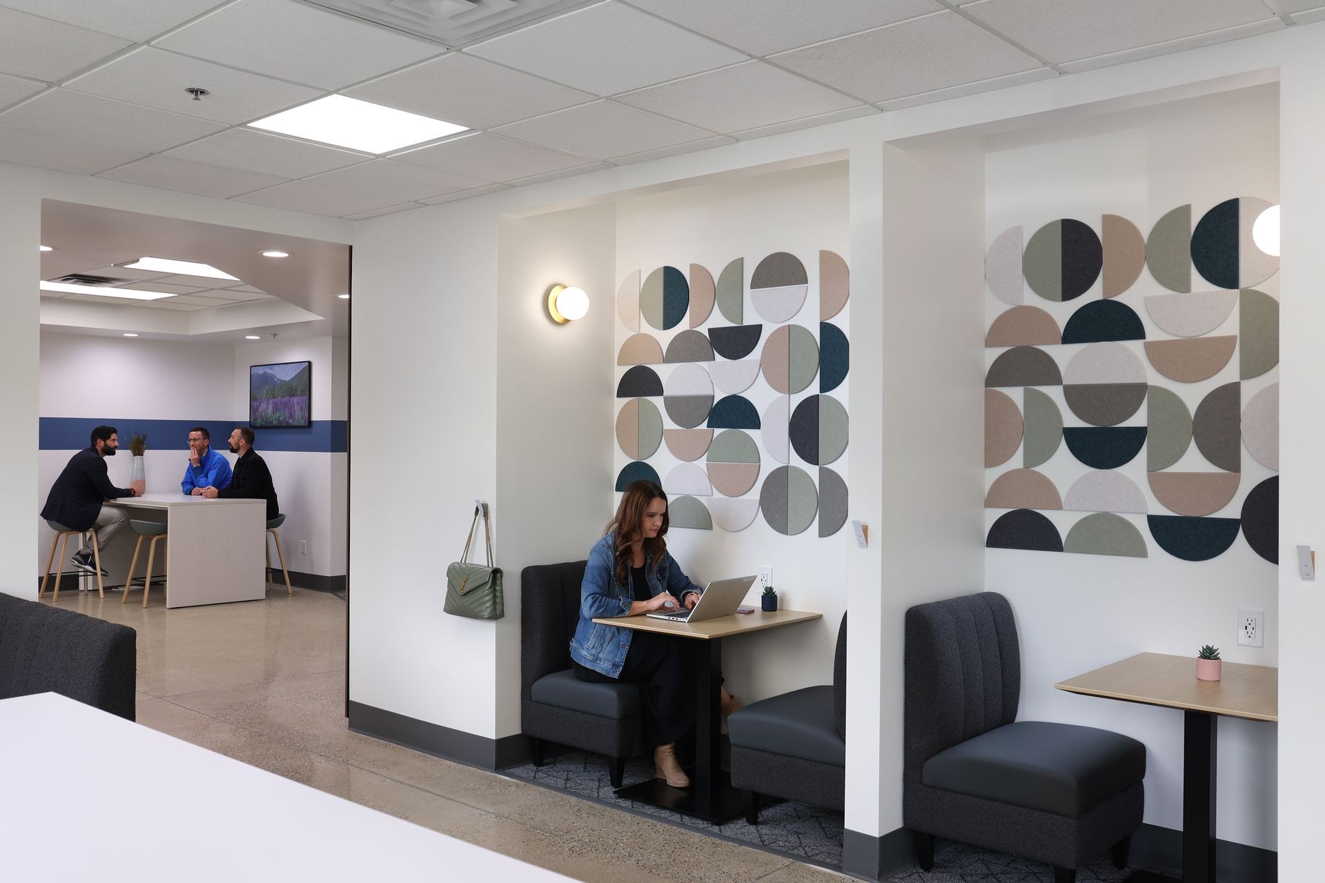 Modern office interior with geometric wall art, seating areas, and individuals working and having a meeting.