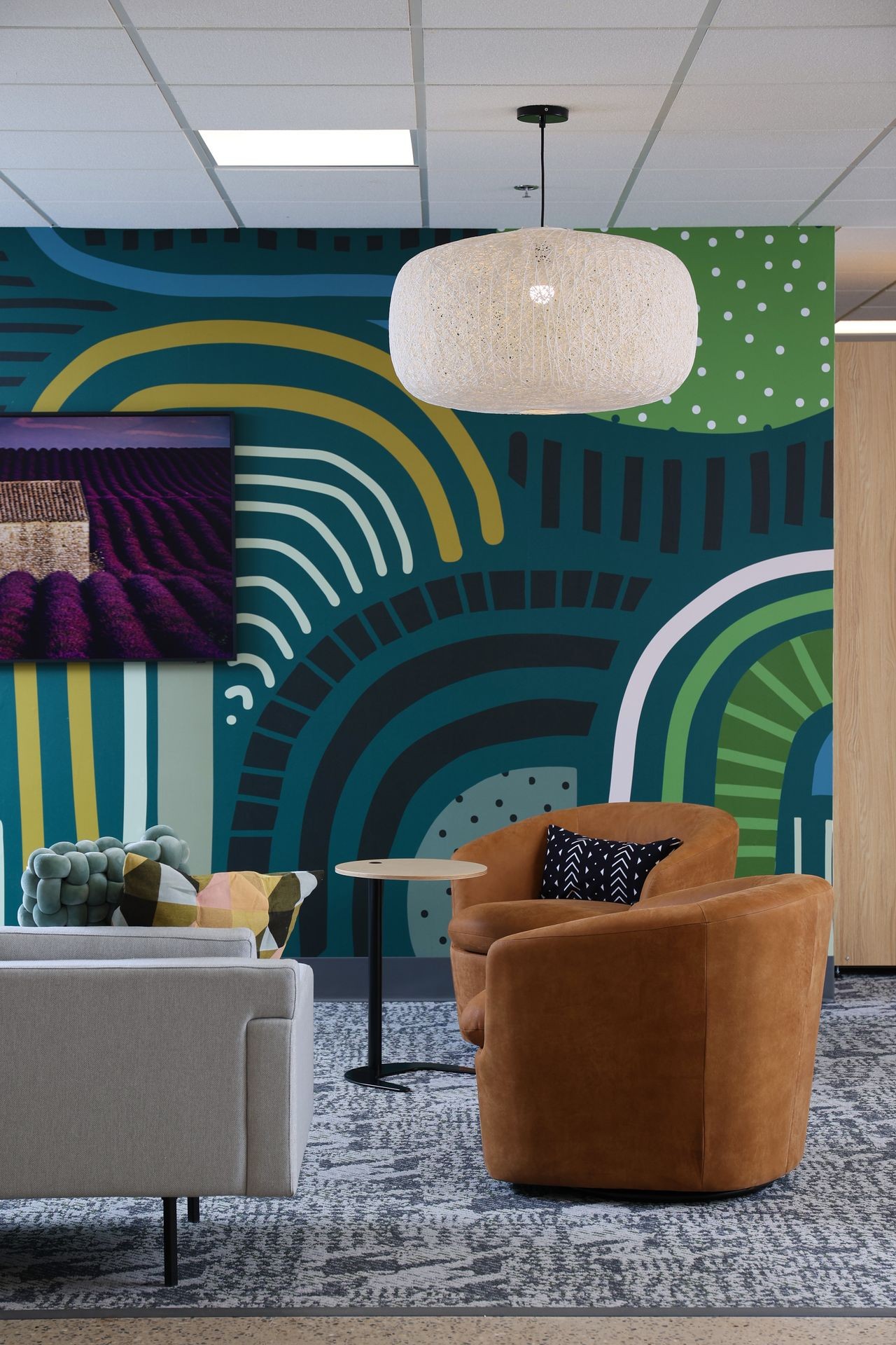 Modern lounge area with patterned wall, brown chair, gray sofa, and a large ceiling light.