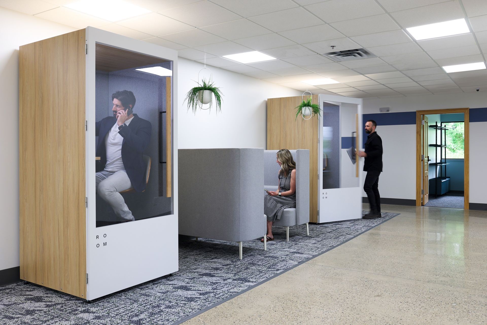 Office space with private phone booths and seating, featuring people working and making calls.