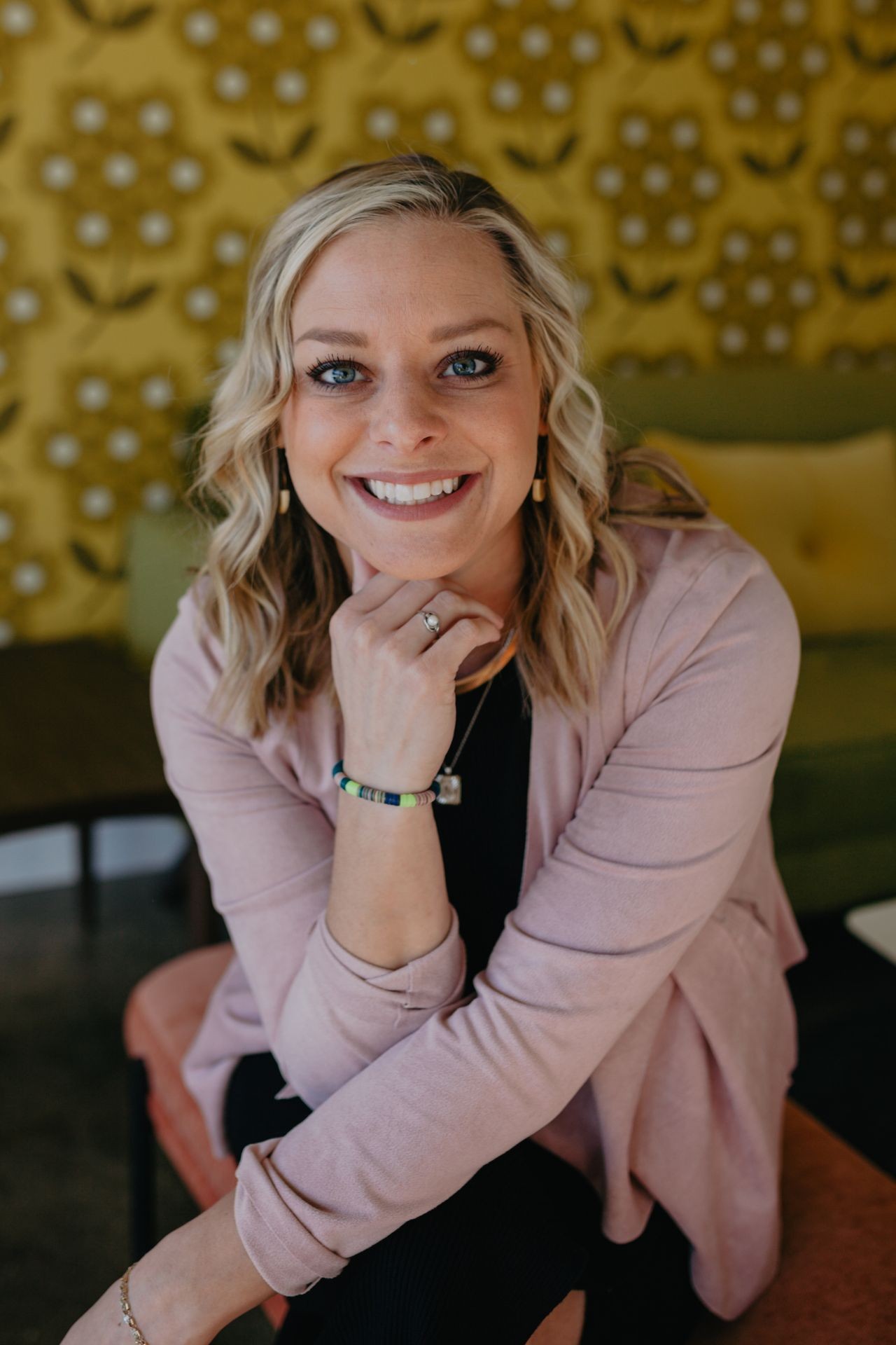 Person wearing a pink cardigan and colorful bracelet, sitting with their hand thoughtfully placed near their chin.