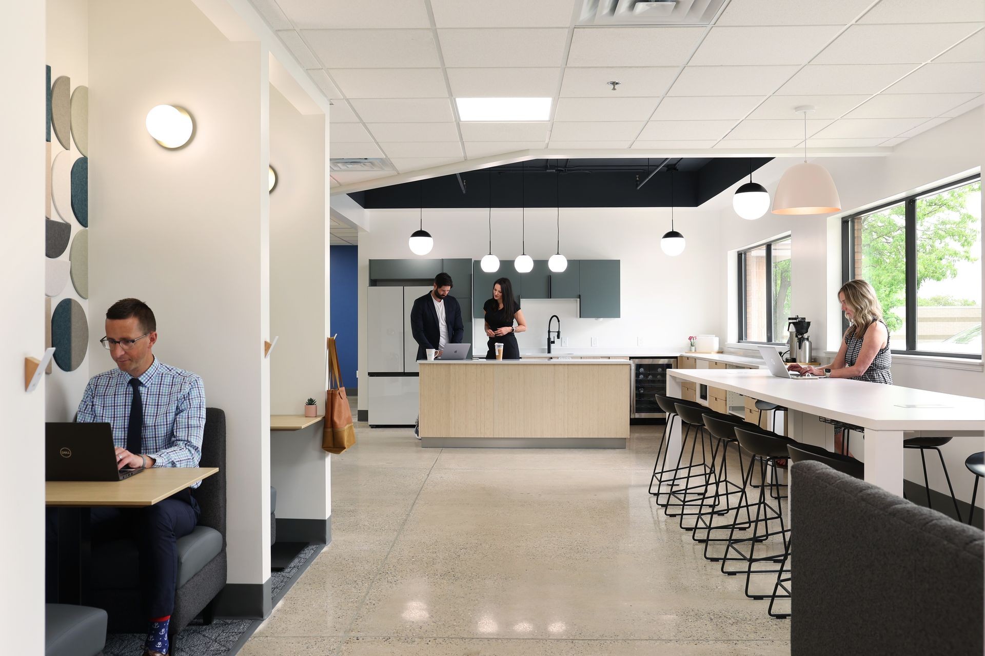 Modern office space with people working at desks, a communal kitchen area and long counter with stools.